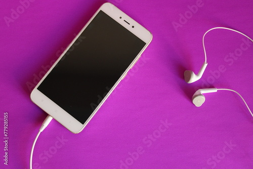 a black phone with earphones on it is laying on a pink surface.