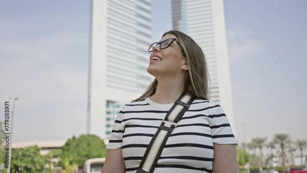 A smiling woman in eyeglasses enjoys her time in downtown dubai, surrounded by modern skyscrapers A smiling woman in eyeglasses enjoys her time in downtown dubai, surrounded by modern skyscrapers