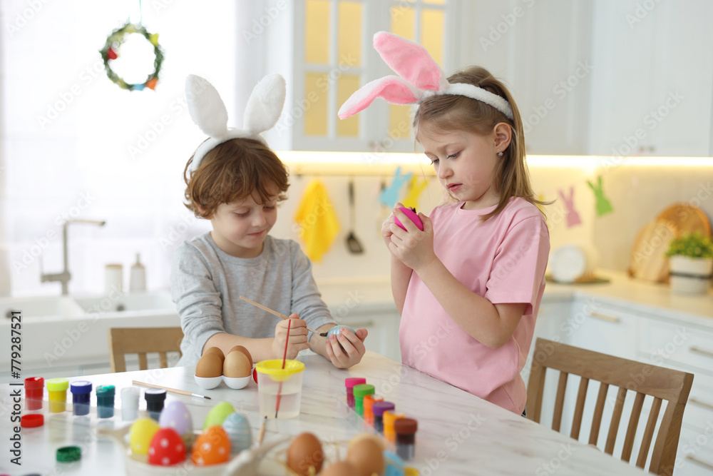 Easter celebration. Cute children with bunny ears painting eggs at white marble table in kitchen Easter celebration. Cute children with bunny ears painting eggs at white marble table in kitchen
