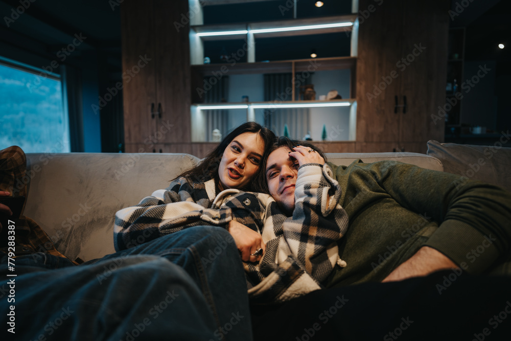 Intimate moment of a young couple snuggled up on a sofa covered with a plaid blanket in a modern living room setting.