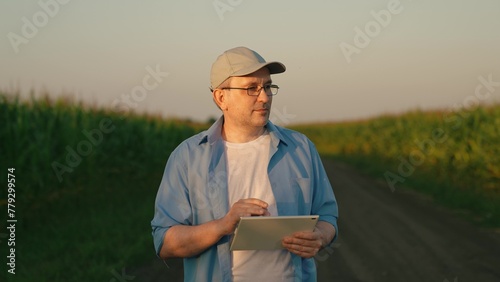 Farmer goes out from corn field after corn harvest inspection. Agronomist prepares for report on tablet about corn checking. Man in glasses emerges from corn field following thorough examination