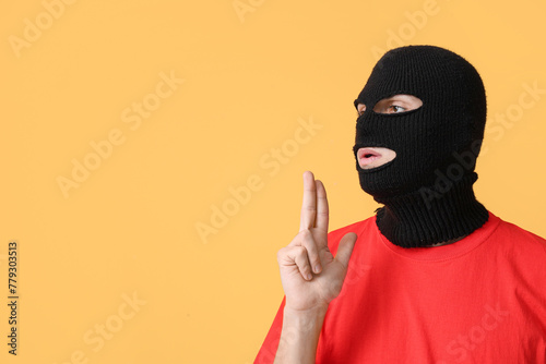 Handsome young man in balaclava showing gun gesture on yellow background
