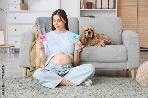 Beautiful pregnant woman holding papers with gender and cocker spaniel on sofa at home