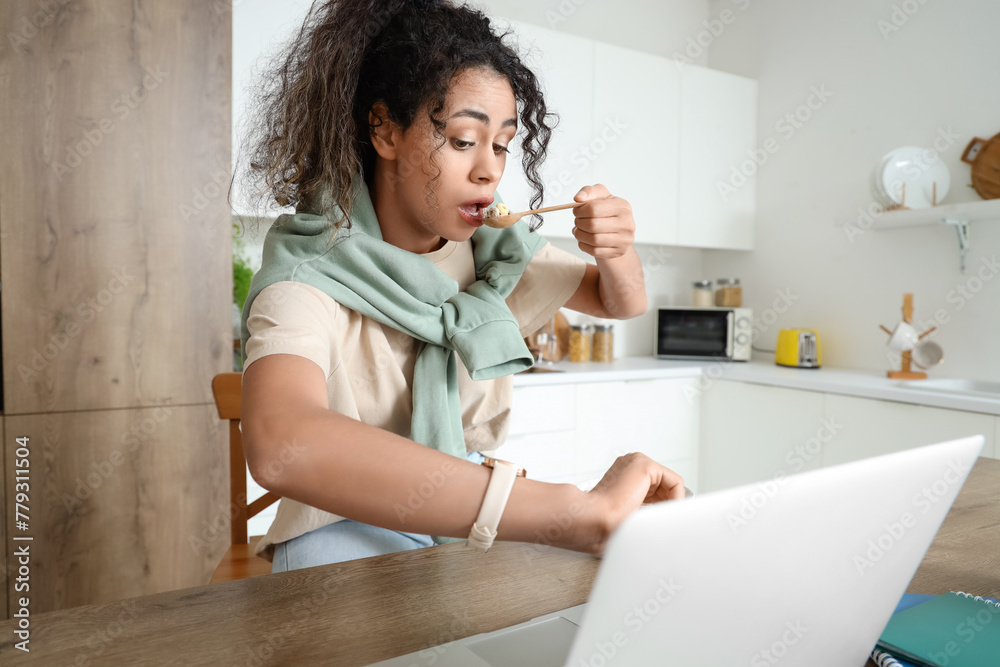 Hurrying young African-American woman eating breakfast and looking at wristwatch in kitchen Hurrying young African-American woman eating breakfast and looking at wristwatch in kitchen