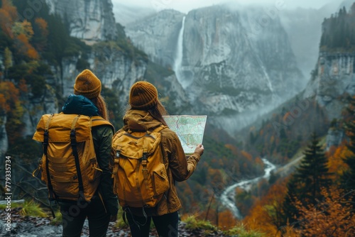 Two hikers with yellow backpacks stand overlooking a grand waterfall in an autumn-hued valley, consulting a map.