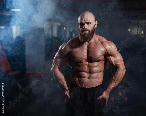 Muscular bald man posing shirtless. Bodybuilder showing off his shape in the gym. 