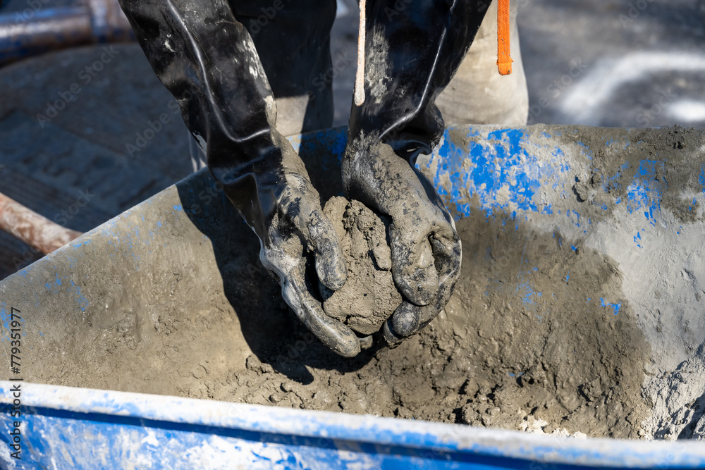 Obraz premium Closeup of a construction worker with black rubber gloves mixing up cement by hand in a wheelbarrow 