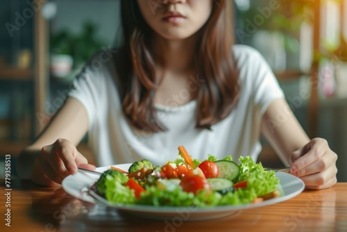 An Asian young girl is sitting at the table  and in front of her is a plate full of vegetables and salad.