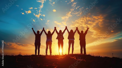 A group of people are standing together in a field, holding hands and looking up at the sky. The sky is filled with clouds and the sun is setting, creating a warm and peaceful atmosphere