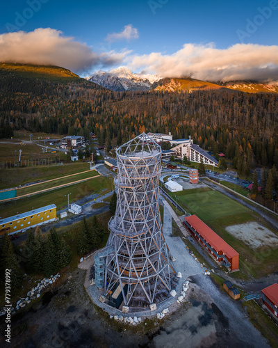 Strbske Pleso, Slovakia - Aerial panoramic view of the sightseeing tower by Strbske Lake with the High Tatras at background on an autumn afternoon at sunset with warm sunlight, blue sky and clouds