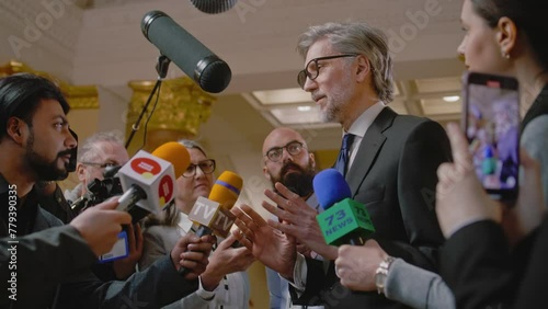 Politician answers press questions and gives interview on television political program. Mature diplomat surrounded by crowd of journalists in government building. Press conference. Inspirational