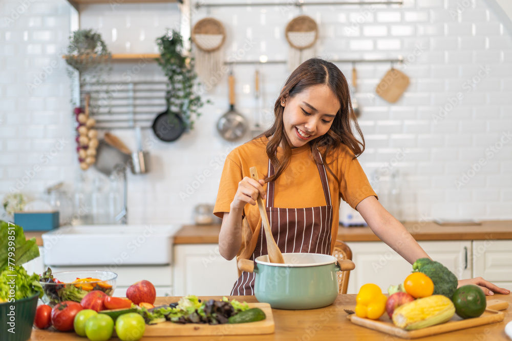 Young woman standing near stove and cooking, housewife, meal, chef, food.Happy woman looking and smelling tasting fresh delicious from soup in a pot with steam at white interior kitchen