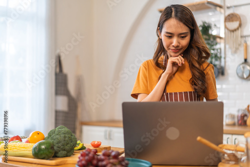 Asian young woman holds a wooden spoon with online audience or simply enjoying the cooking process, health, fruit, freshness, and organic living, digital recipe platform, eating, healthy at kitchen