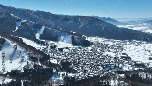 Aerial orbiting shot of Japans Nozawaonsen Mountain Ski Resort Village. Camera orbits the ski village resort with mountains and ski fields in background. Clear Winter Day photo