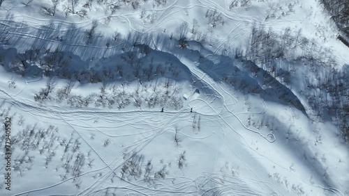 Father and Son Walk through thick snowy mountain side. Top down aerial shot looking down from above as the pair hike along he snowy covered mountain. Japan Nozawaonsen Mountains, clear winter day photo