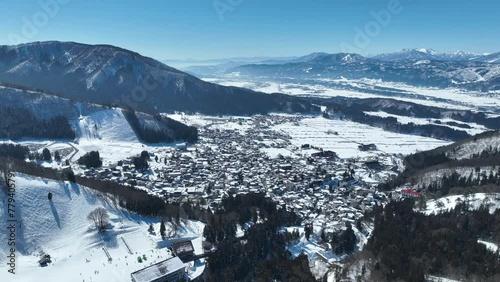 Aerial establishing shot of Japans Nozawaonsen Mountain Ski Resort Village. Camera orbits ski village resort with the mountains and ski fields in background. Clear Winter Day photo