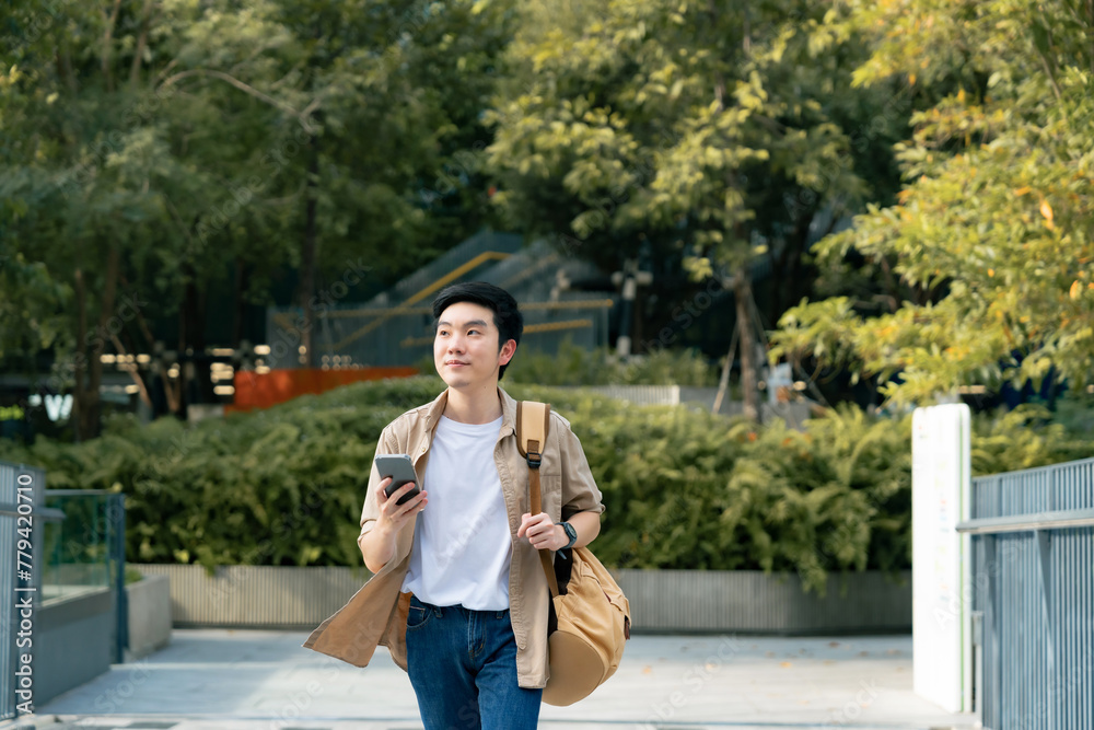 Portrait of handsome Asian student using smartphone. A young man walking outdoor happy smiling with holding mobile phone