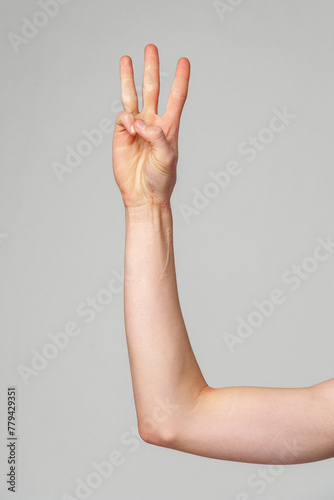 Hand Gesturing Number Three Against a Plain Background in Natural Light