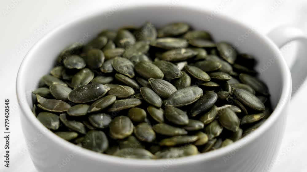 Full white ceramic cup of green peeled pumpkin seeds close up. Healthy raw ingredients. Rotation Full white ceramic cup of green peeled pumpkin seeds close up. Healthy raw ingredients. Rotation