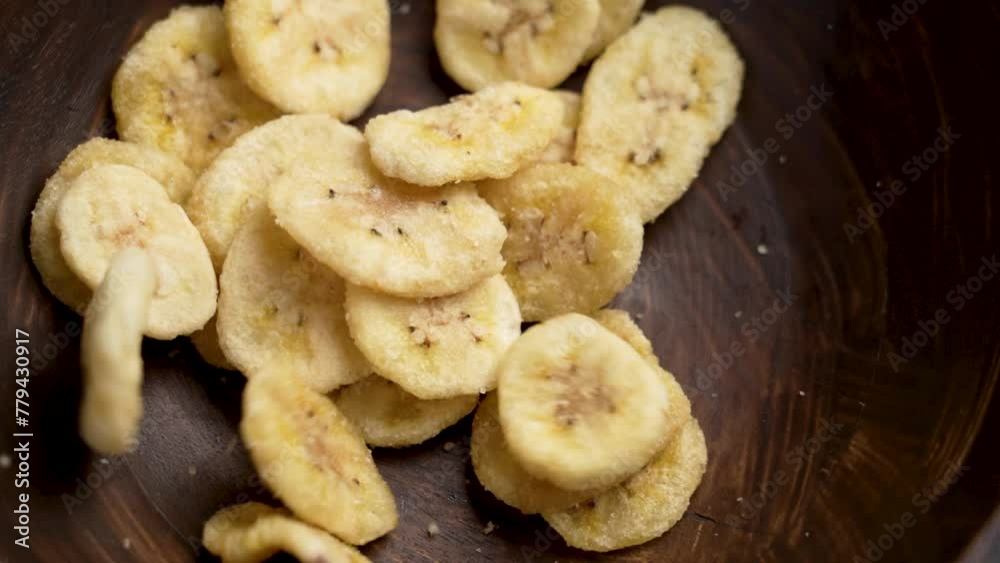 Dried banana chips falling into a rustic wooden bowl in slow motion. Dehydrated nutritious sliced fruit. Rotation Dried banana chips falling into a rustic wooden bowl in slow motion. Dehydrated nutritious sliced fruit. Rotation