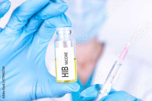 Text HIB VACCINE of is written on a bottle with the background of a doctor with a syringe in a medical glove and mask. Medical concept. photo