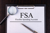 Text FSA is written on a notebook with a pen and a magnifying glass lying on the table. Business concept.