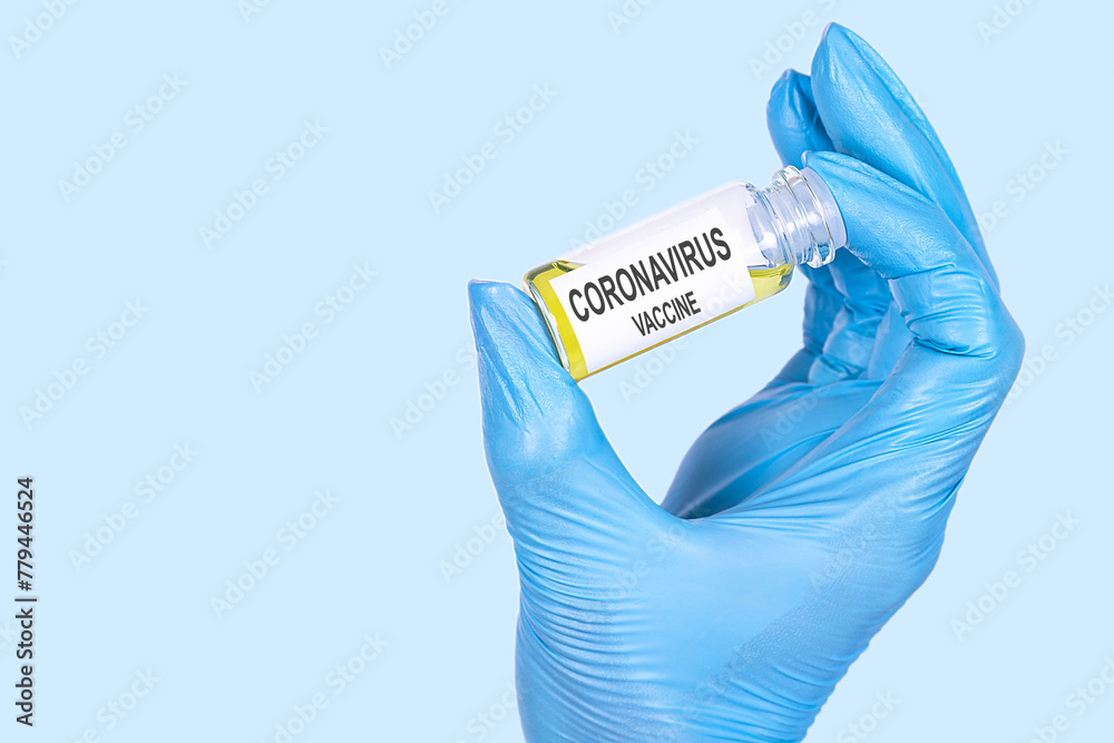 CORONAVIRUS VACCINE text is written on a vial whose ampoule is held by a hand in a medical disposable glove. Medical concept.