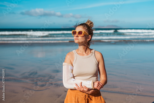 Woman with broken arm on beach. Arm cast, injured during family vacation in holiday resort. Concept of beach summer vacation.