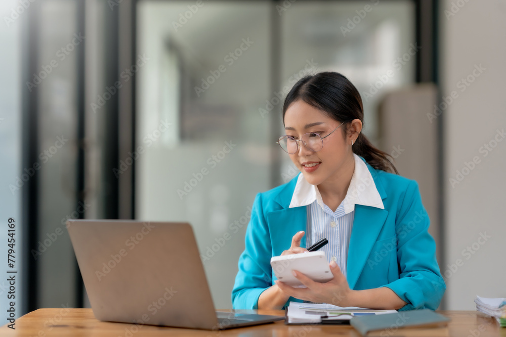 Young Asian businesswoman using a calculator to calculate business principles. Accounting statistics concept at the office. Young Asian businesswoman using a calculator to calculate business principles. Accounting statistics concept at the office.