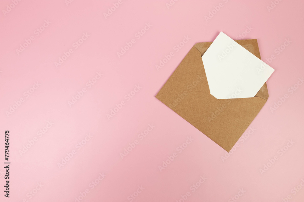 Top view of brown kraft envelope, white card on pink background. Post flat lay. Copy space.
