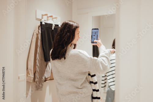 Korean teenage girl takes a selfie in new clothes in the mirror and sends it to her friend via phone in a shopping mall. Retail and consumerism. Sale promotion and shopping concept. Part of a series