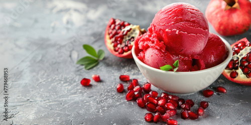 A sumptuous bowl of pomegranate sorbet is elegantly presented with fresh pomegranate seeds and leaves on a textured grey background. photo
