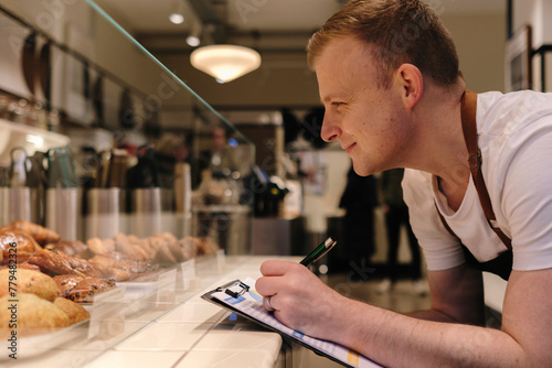 Smiling baker taking inventory on clipboard in bakery photo