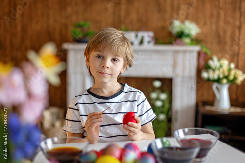 Beatiful blond child, boy, coloring and painting eggs for Easter at home © Tomsickova