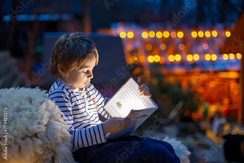 Beautiful blond child, boy, reading a book at night with flashligh, sitting on the stairs in garden photo