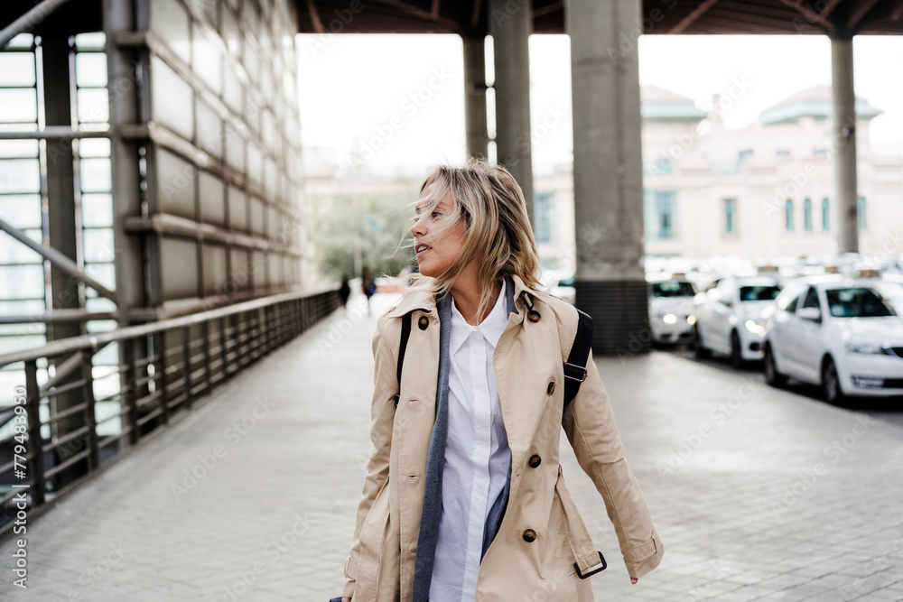 Woman wearing long coat walking on sidewalk at train station Woman wearing long coat walking on sidewalk at train station