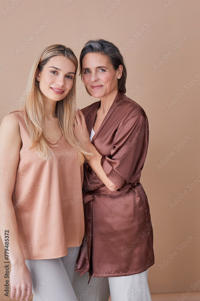 Beautiful mother and daughter standing against beige background Beautiful mother and daughter standing against beige background