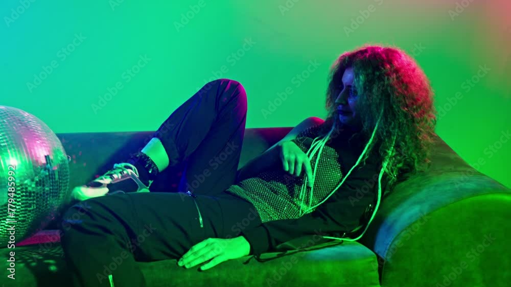 Woman sitting on couch with disco ball Scene is set in dimly lit room