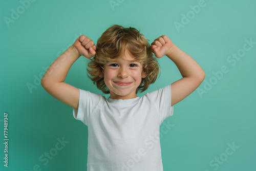 A happy and healthy young boy is standing and flexing his arms muscle.