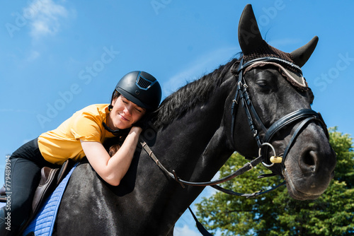 Smiling instructor with eyes closed riding black horse on sunny day photo