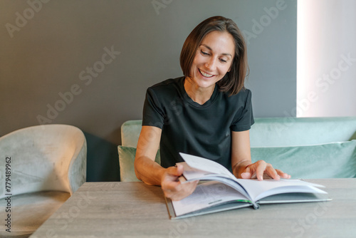 Happy businesswoman turning pages of magazine in cafe photo