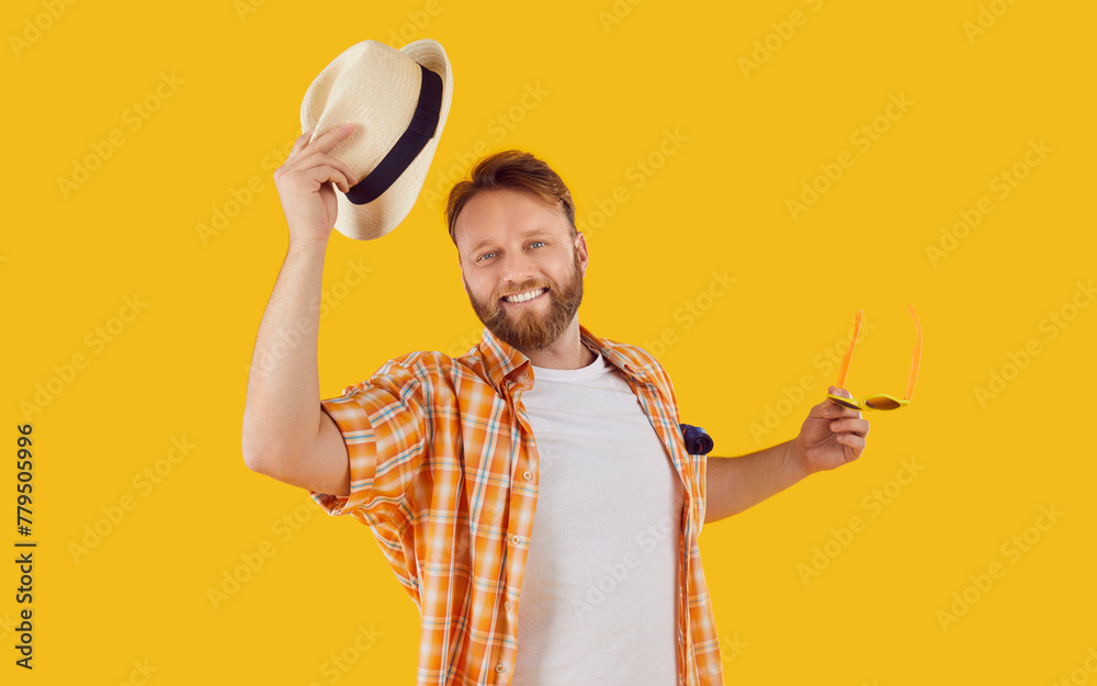 Portrait of a smiling man in summer attire, joyfully removing hat in greeting against an orange background. This image captures the essence of a happy vacation or holiday moment in the summer. - obrazy, fototapety, plakaty 