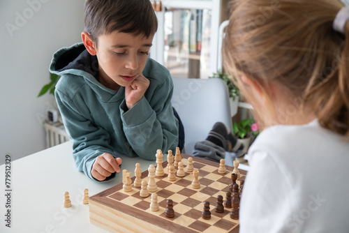 Primary school boy and girl very focused playing a game of chess at home. Hobbies for children, education without screens.