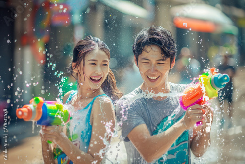 Happy traveler asian man and woman wearing summer shirt holding colourful squirt water gun over blur city, Water festival holiday concept photo