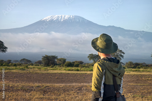 man walks against backdrop of Kilimanjaro. African walking safari. male traveler with backpack looking at amazing mountains and forest, wanderlust travel concept, copy space photo