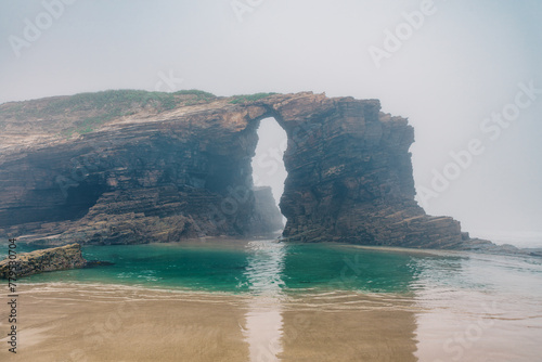 Cathedrals beach in Galicia, Spainn. Foggy landscape with Playa de Las Catedrales Catedrais beach in Ribadeo, Lugo on Cantabrian coast. Natural archs of Cathedrals beach. Moody rock formations photo