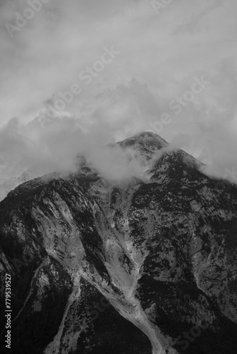 Vertical of a mountain range covered with snow and clouds shot in grayscale