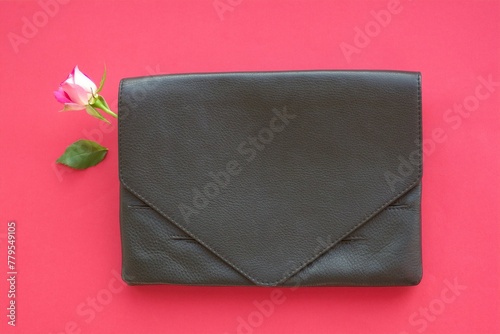 elegant black leather clutch with bright pink rose bud and separated green leaf on a background of pink paper