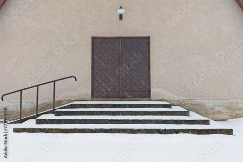 Old weatherd wooden door on a stone building with stairs and handrail in winter with snow on the ground. photo