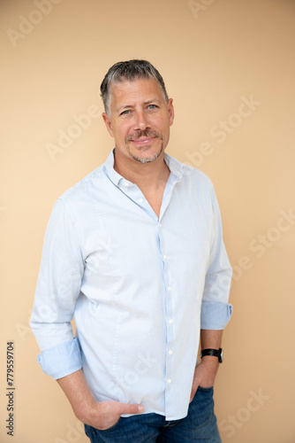 midage man man with grey hair and beard, wearing light blue shirt, posing in front of brown background